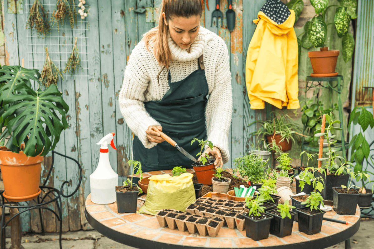 Autossuficiência e conexão com o alimento através do cultivo Jardineira concentrada realizando o plantio de mudas em vasos sobre uma mesa rústica, ilustrando a autossuficiência alimentar e a conexão pessoal com a natureza.